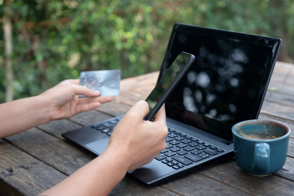 Smartphone and credit cards in hand with laptop and coffee on wo